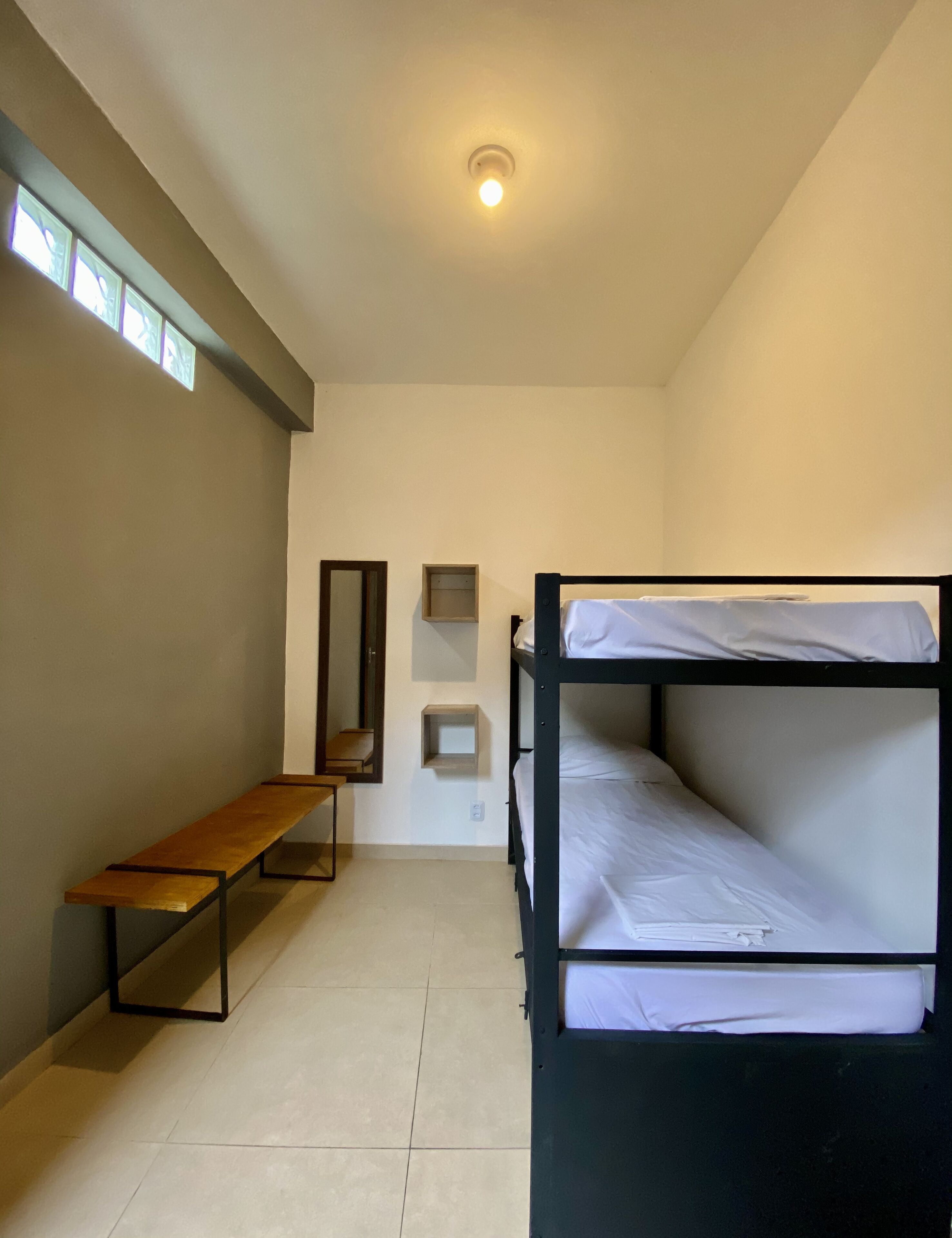 Un dormitorio con literas, un banco de madera, un espejo pequeño y una estantería.