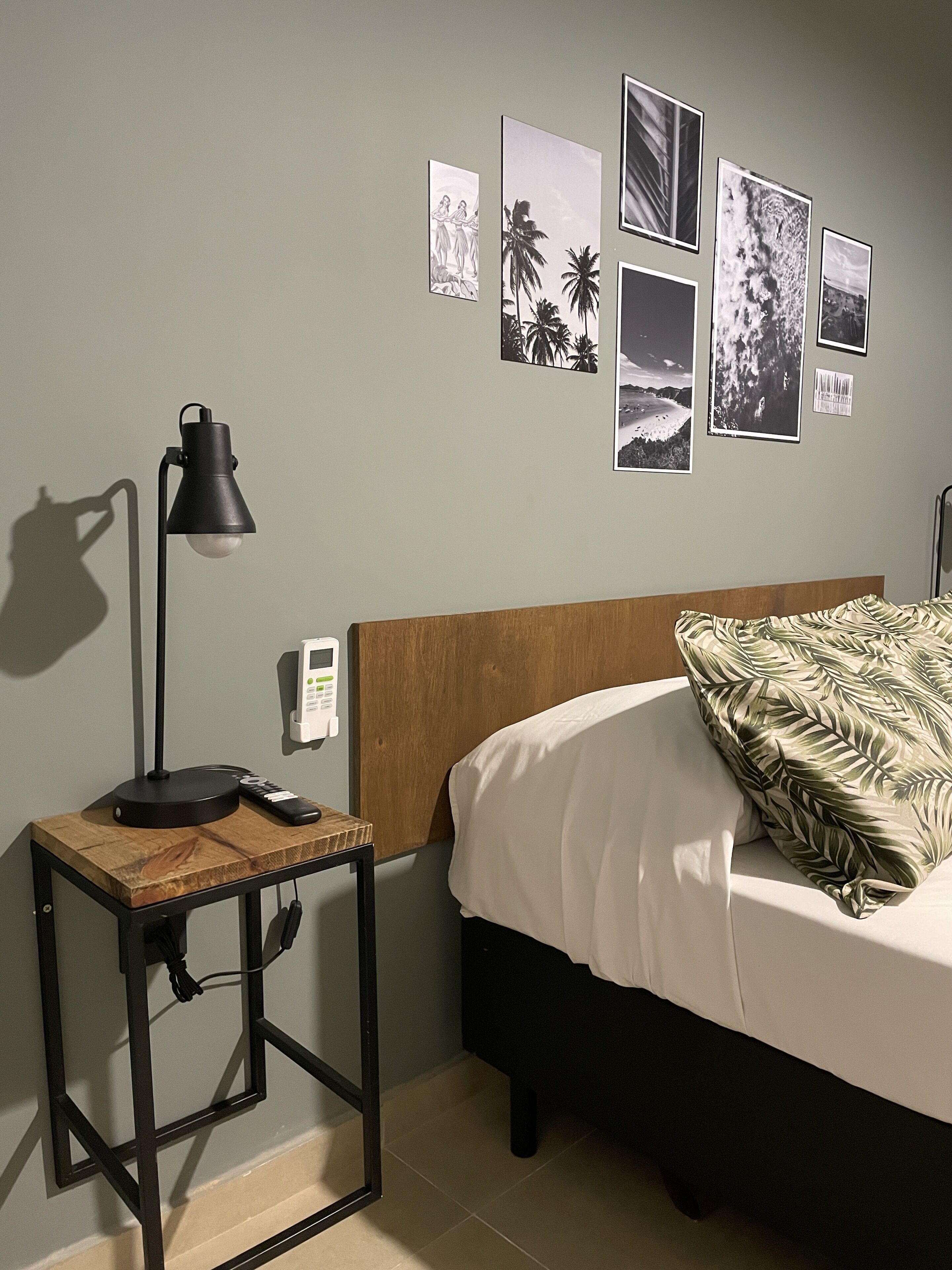 Quarto com cama, mesa de cabeceira com abajur, relógio de parede e várias fotos emolduradas.