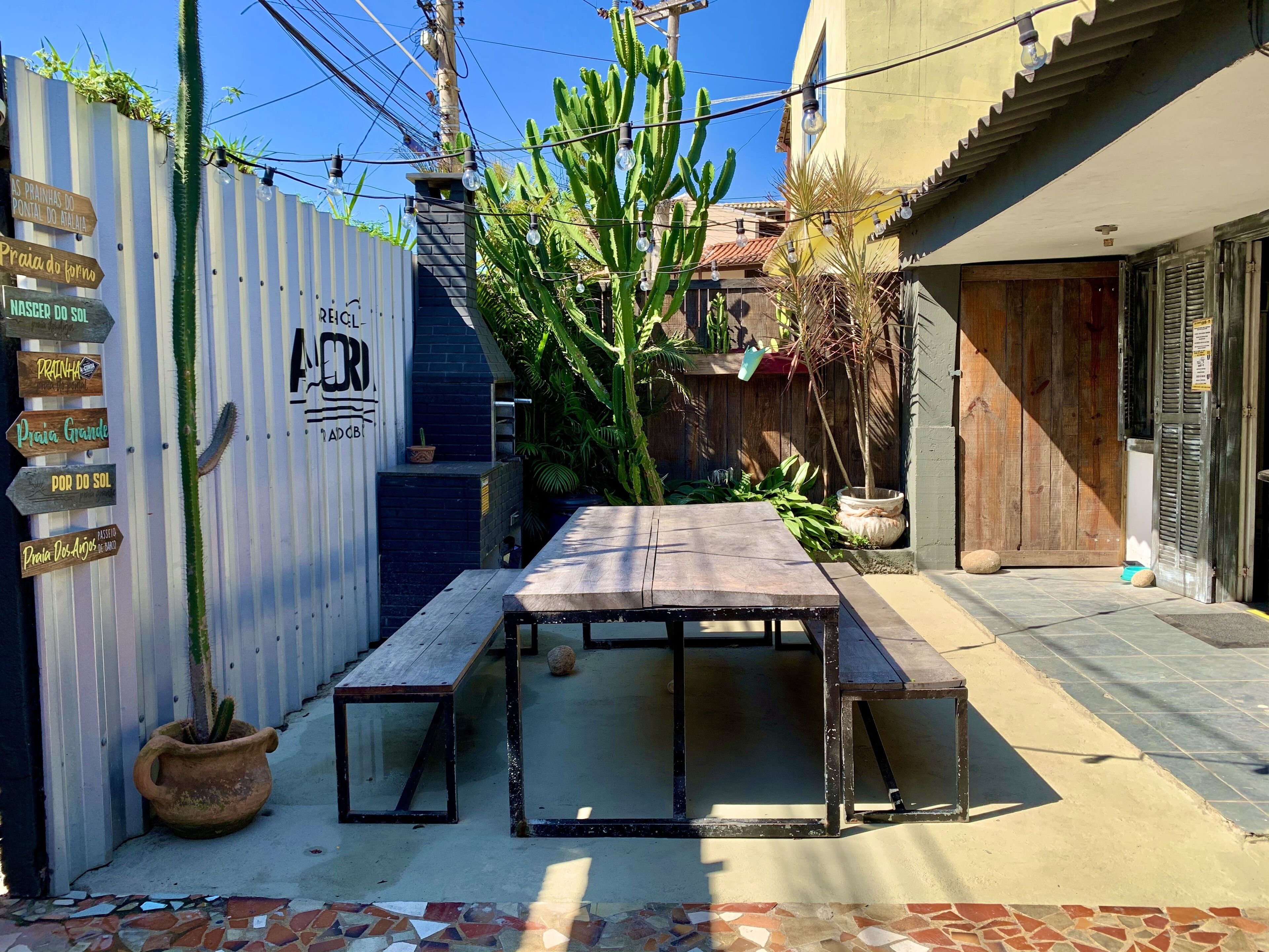 A patio with a wooden table and benches, surrounded by potted plants and a cactus.