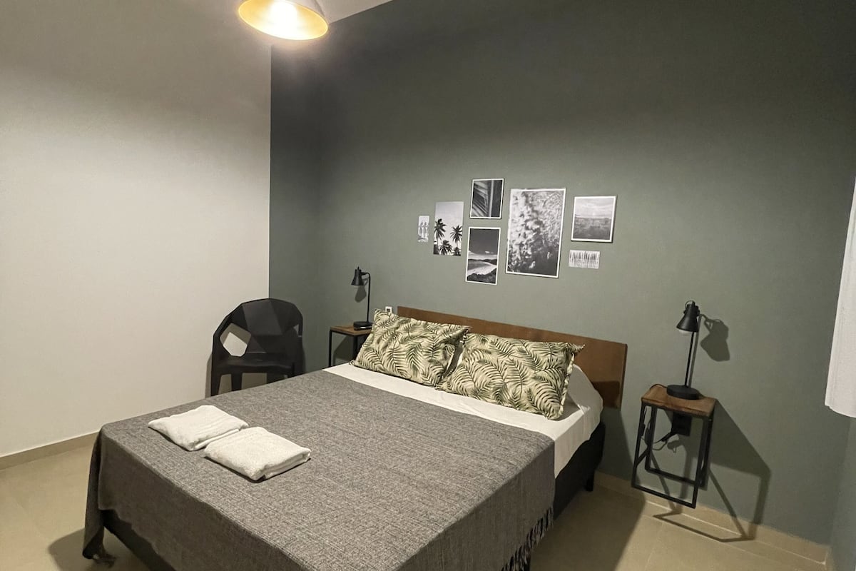 A bedroom with a bed, a chair, a bedside table, a lamp, and wall art.