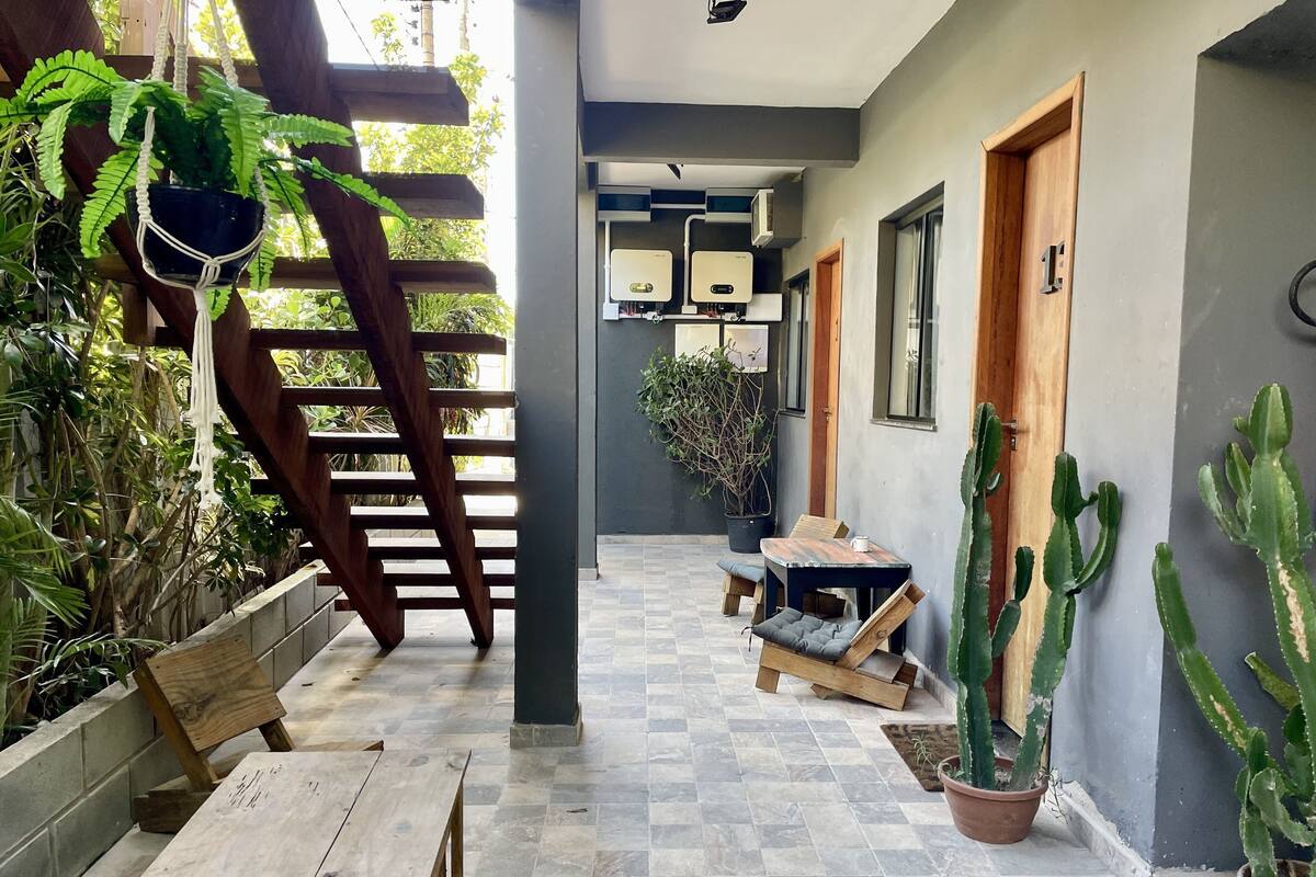 A covered outdoor area with a wooden table and benches, potted plants, and a wooden door.