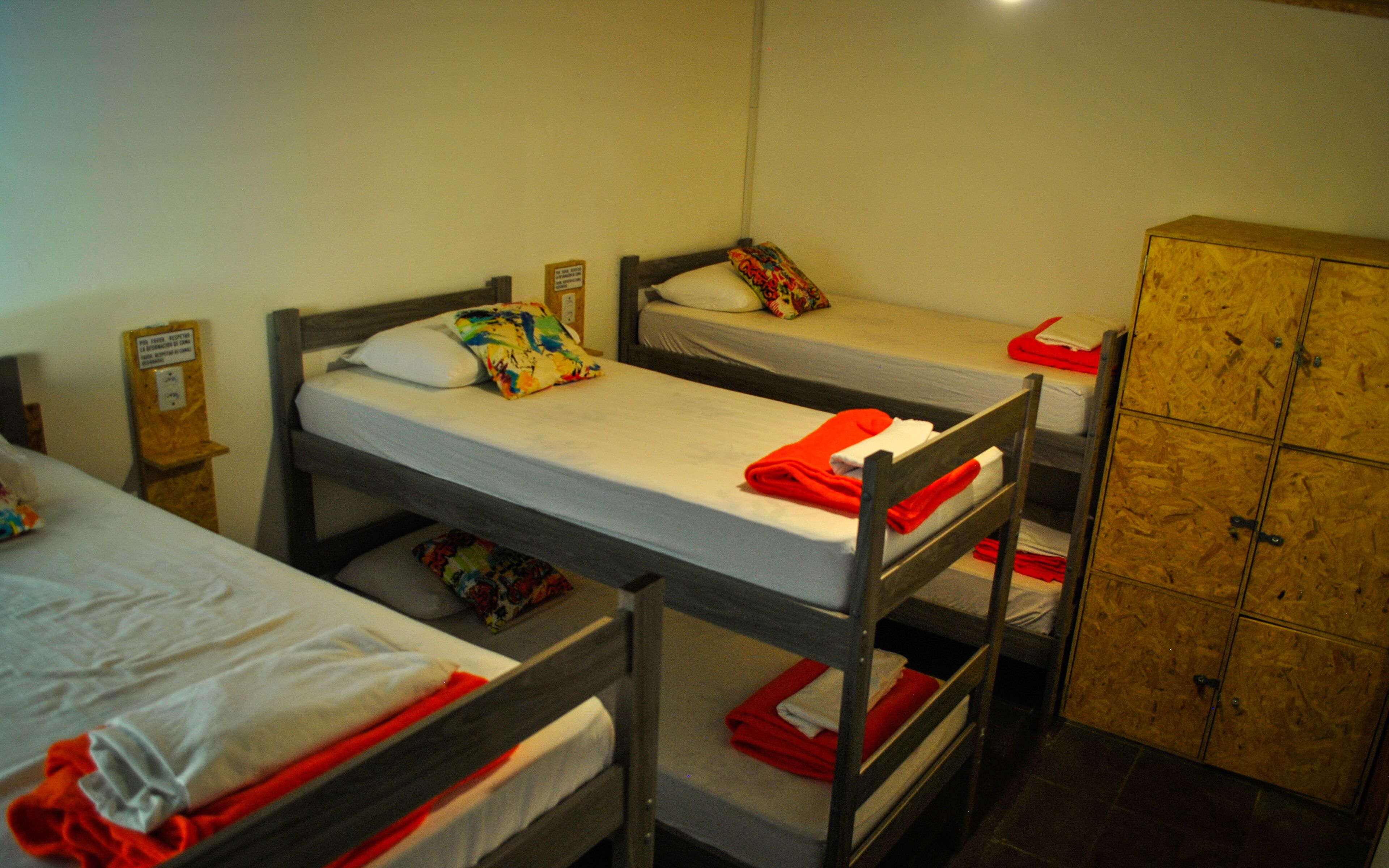 Un dormitorio con literas, un armario de madera y un pequeño estante de madera con un cartel.