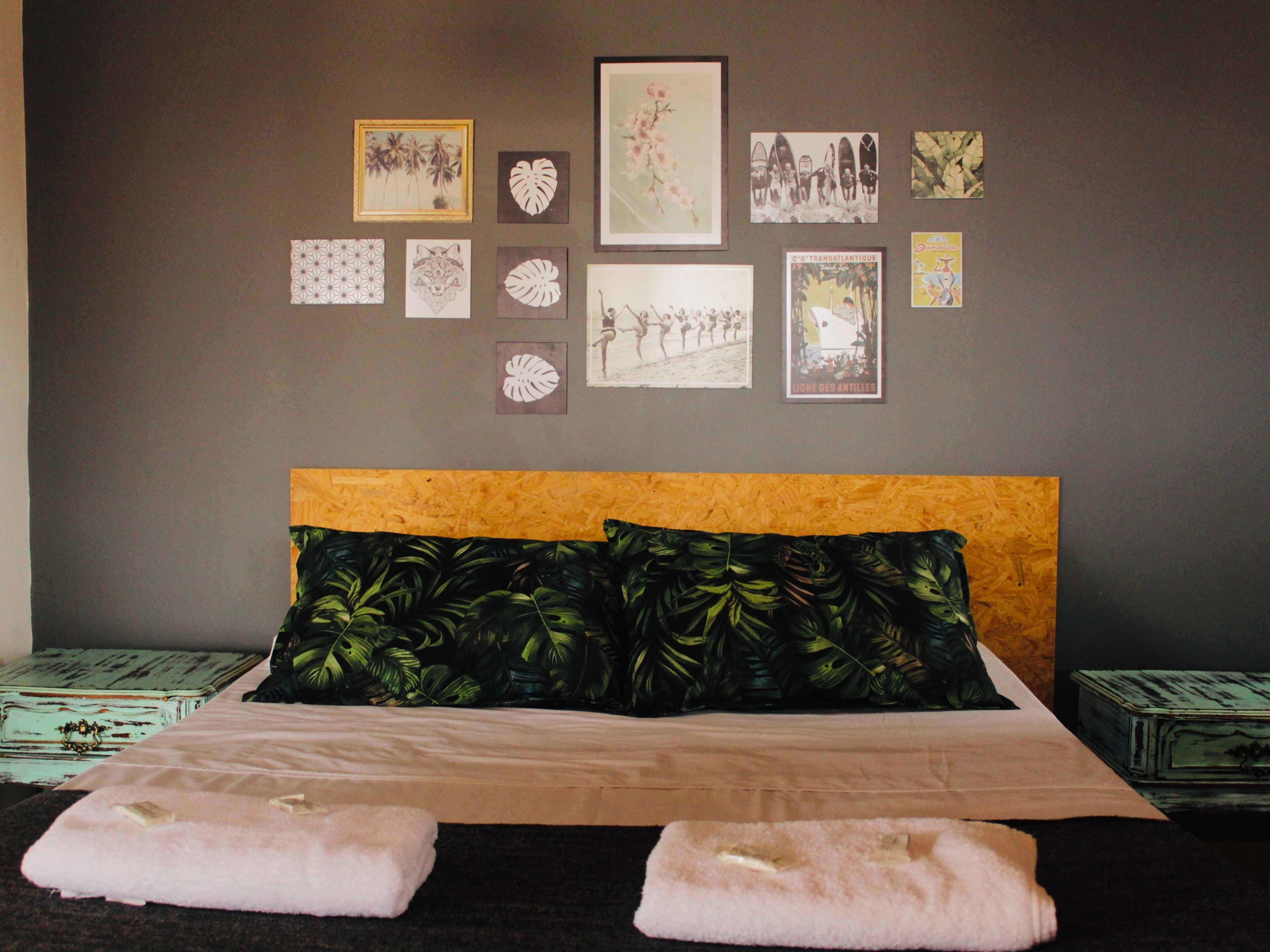 A bedroom with a bed, pillows, and a wall decorated with various framed pictures.