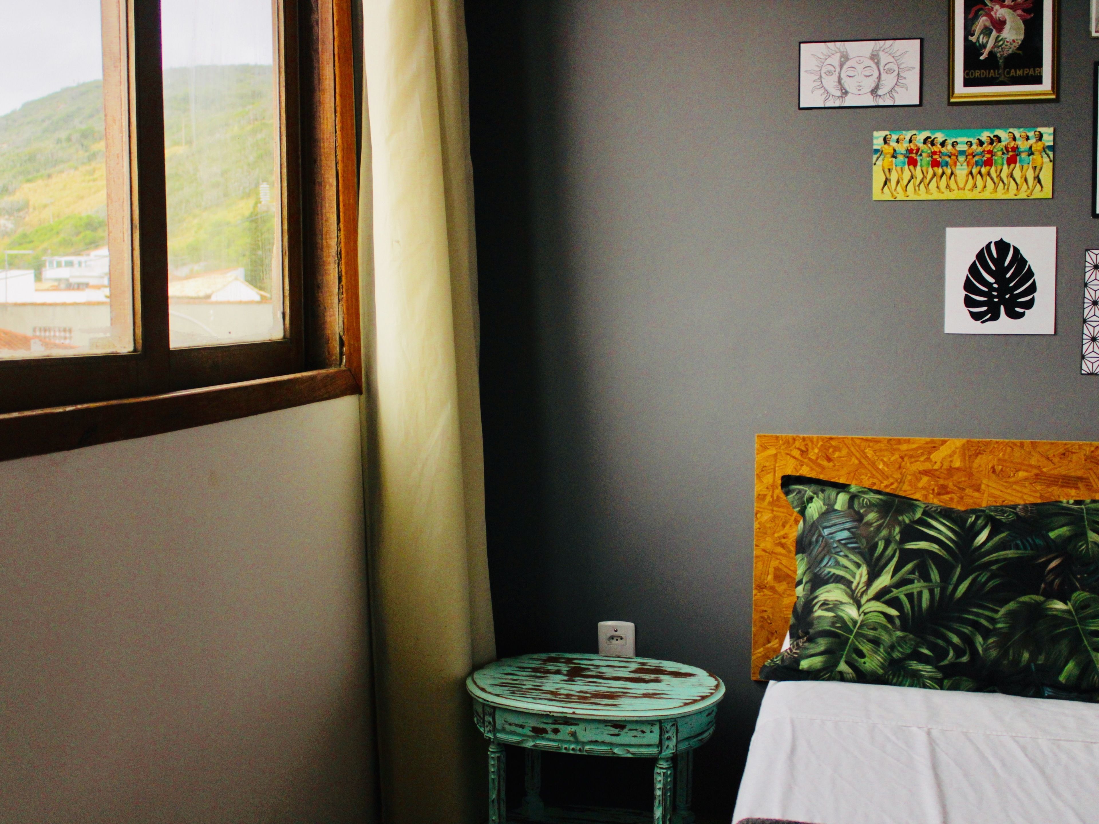Une chambre avec un lit, une petite table, une fenêtre donnant sur des collines et divers éléments de décoration murale.