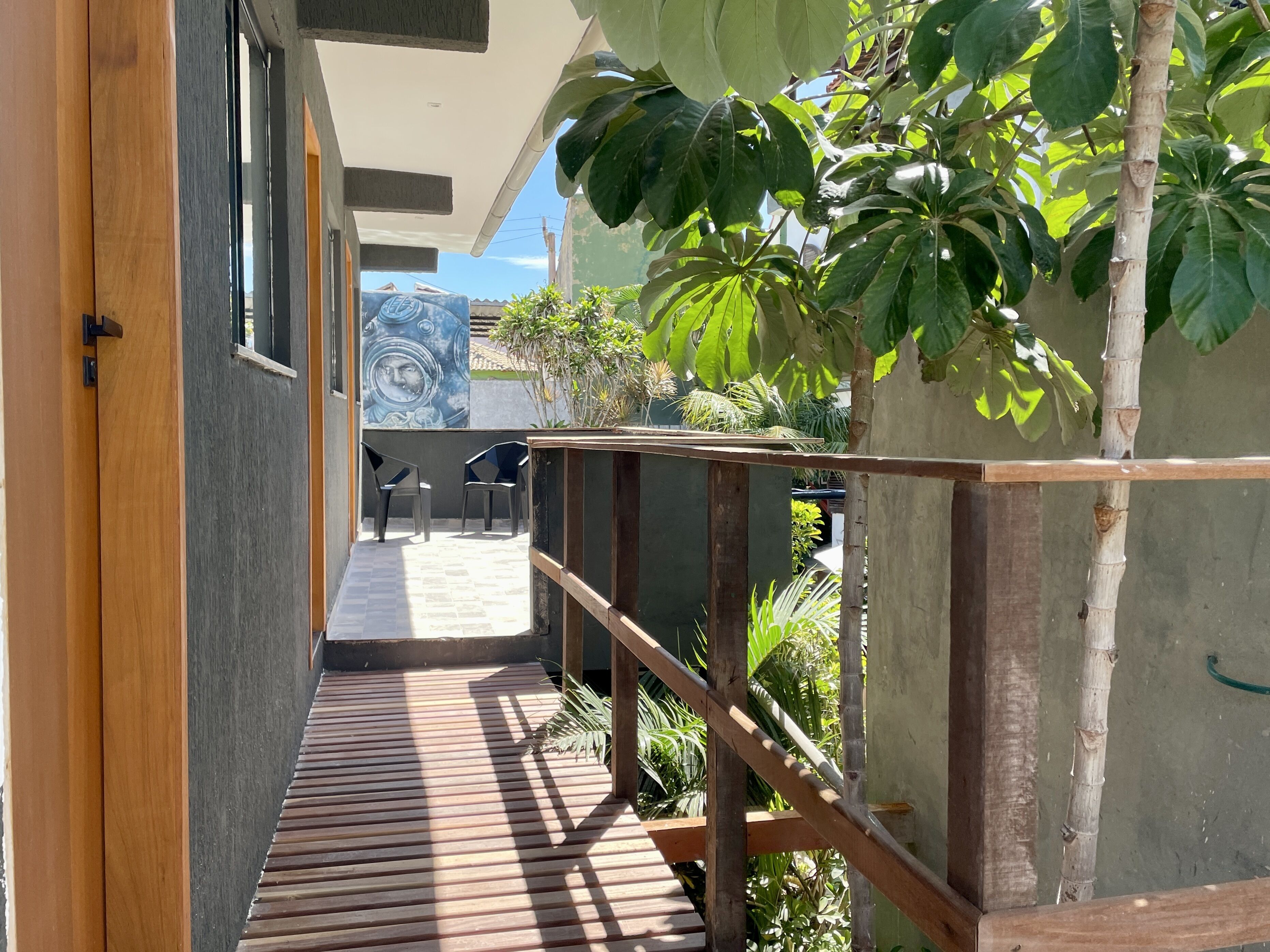 A narrow wooden deck with a metal railing, leading to a covered outdoor seating area with chairs.