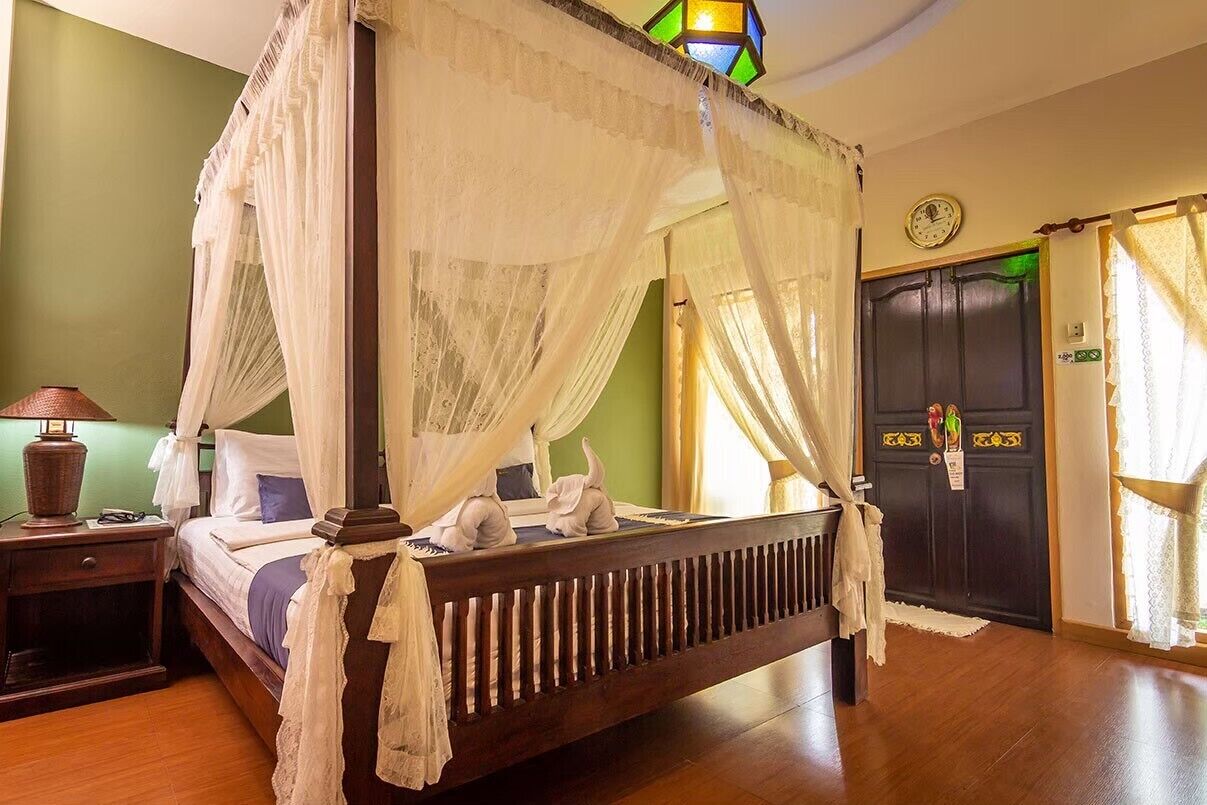 A four-poster bed with a canopy, a nightstand with a lamp, and a dark wooden door with a decorative handle.