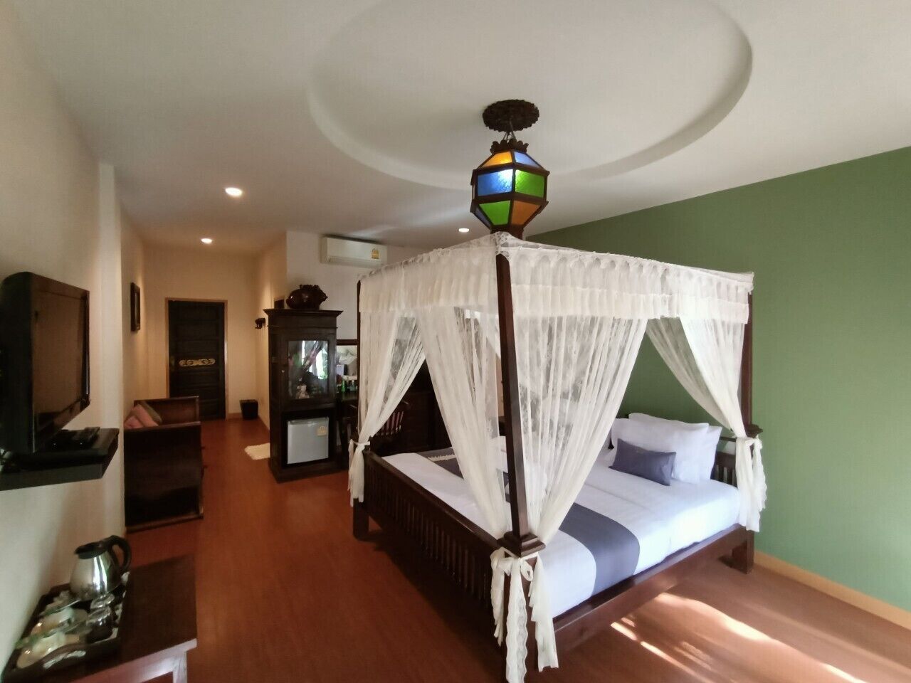 A room with a four-poster bed, a television, a desk, and a cabinet.