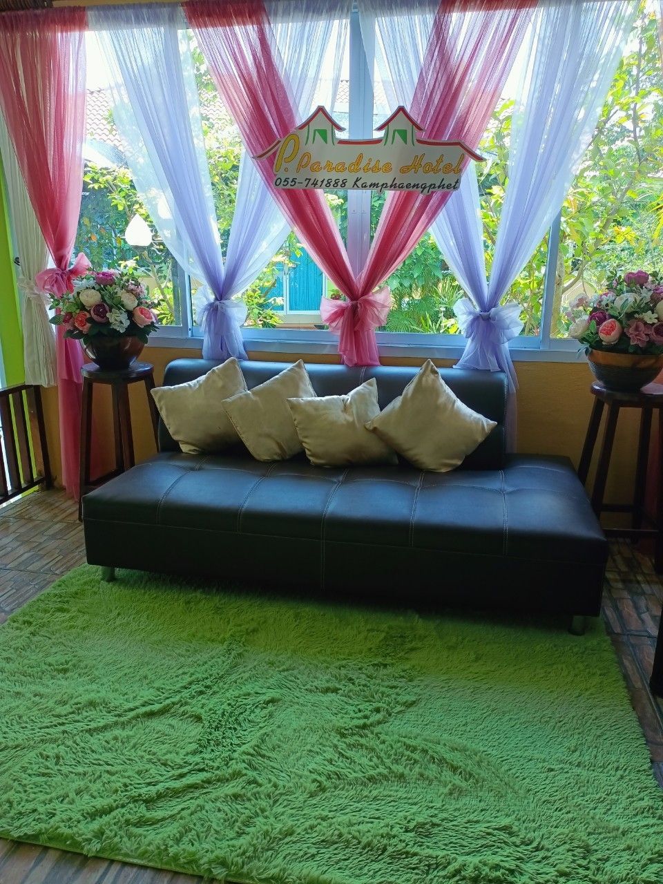 A room with a black sofa, green rug, and a sign above the window.