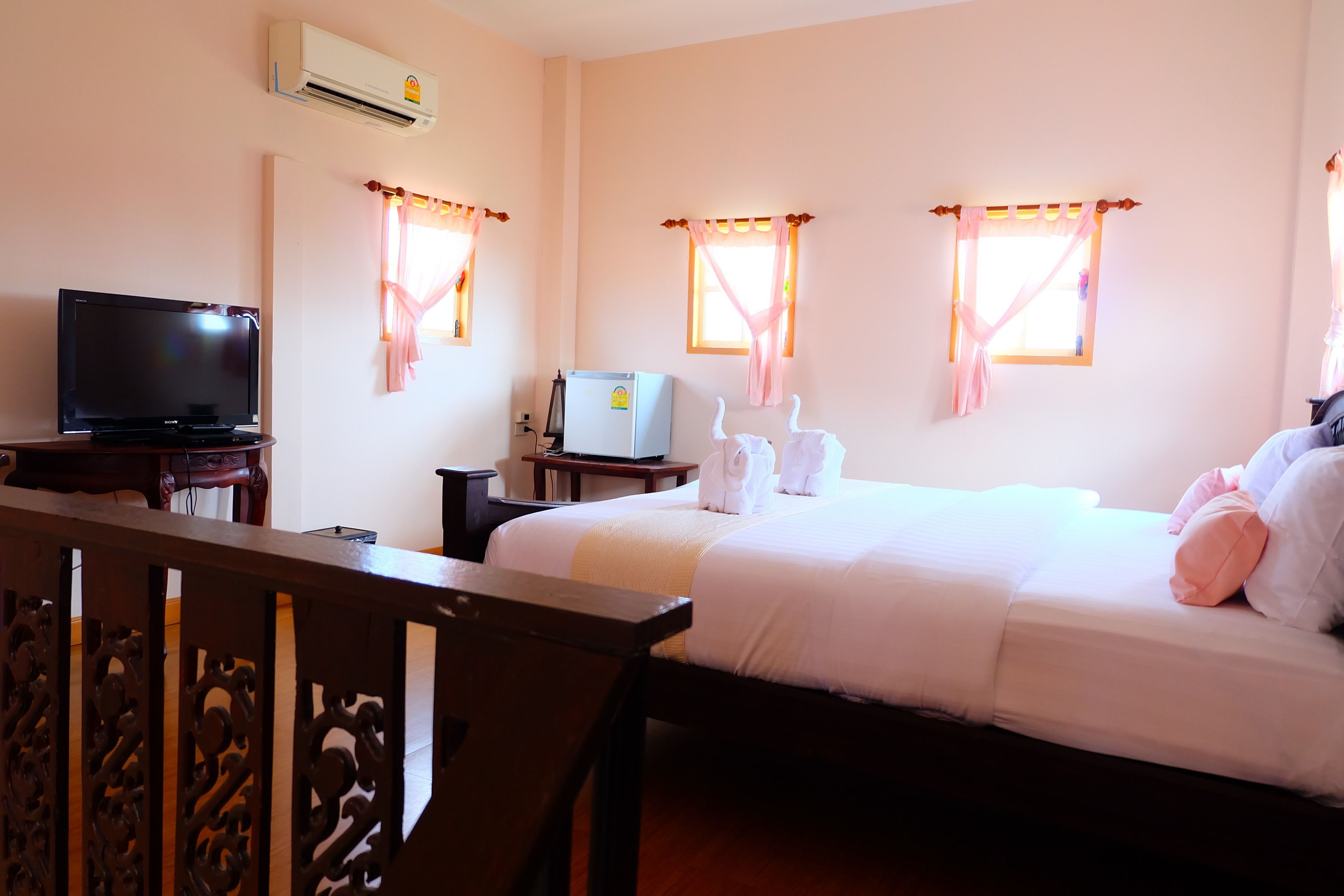 A hotel room with a bed, a television, a refrigerator, and a window with curtains.