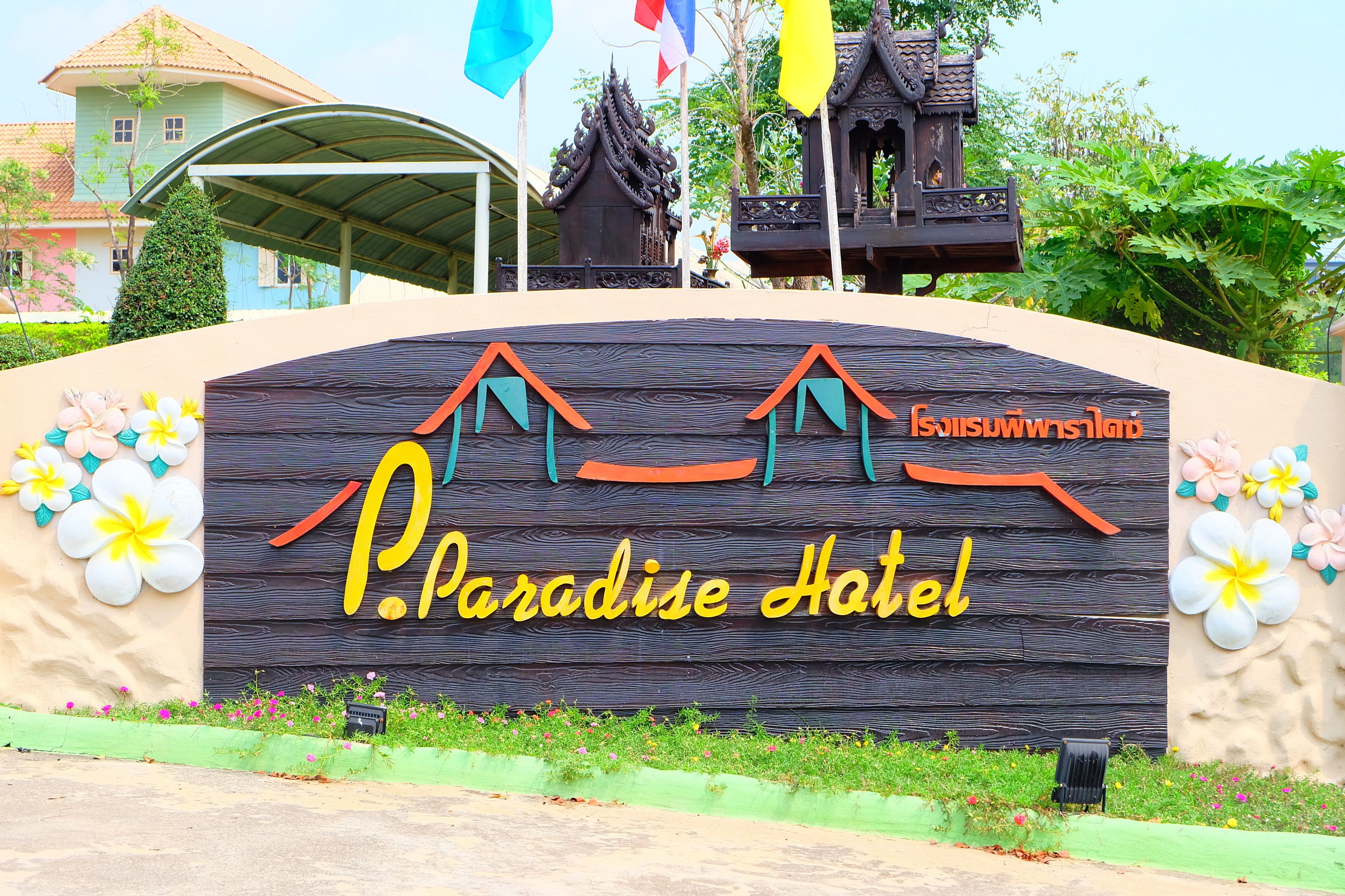 Señal del Paradise Hotel, con fachada de madera, flores decorativas y estilo arquitectónico tradicional tailandés al fondo.