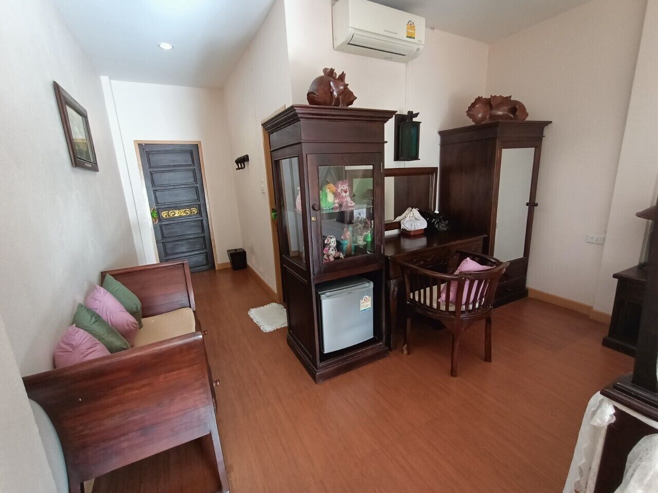 A living room with a wooden sofa, a glass-fronted cabinet, and a dining table with chairs.