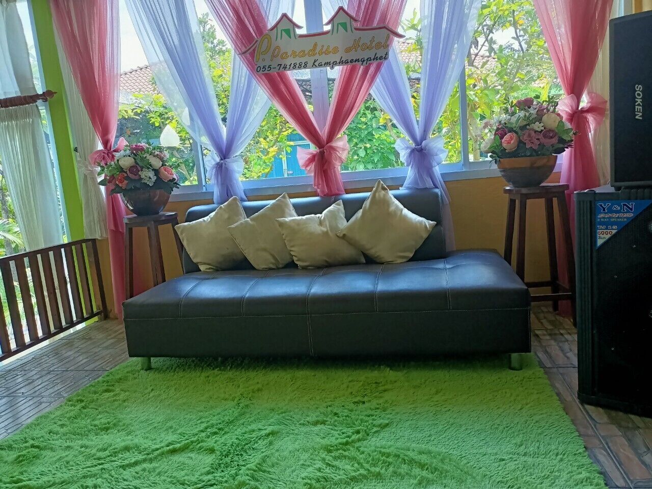 A black sofa with beige cushions, a green furry rug, and a sign reading "Paradise Hotel" in the background.