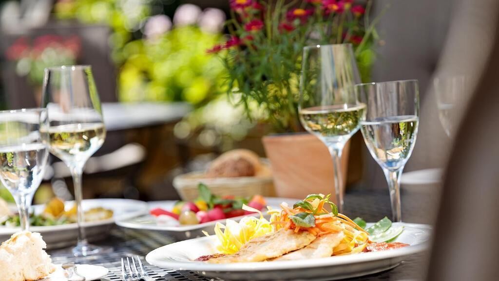 A dining table with plates of food, glasses of white wine, and a vase of flowers.