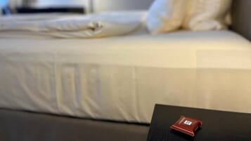 Ein Bett mit weißer Bettwäsche und Kissen, ein schwarzer Tisch mit einem roten Gegenstand darauf und eine Wand mit gerahmten Bildern.