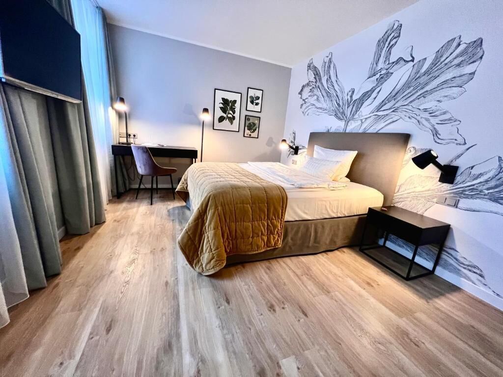 Ein modernes Hotelzimmer mit Bett, Schreibtisch, Stuhl, einer großen Wandmalerei und Holzboden.
