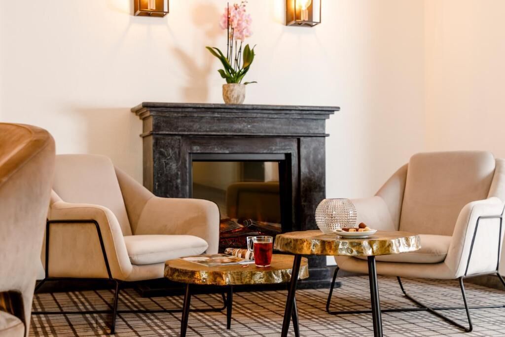 Una habitación con dos sillones, una mesita redonda con una bebida y una chimenea decorada con un florero.