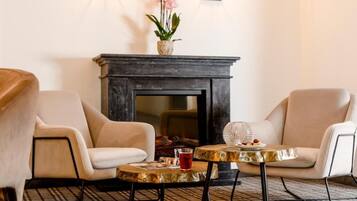 Una habitación con dos sillones, una mesita redonda con una bebida y una chimenea decorada con un florero.