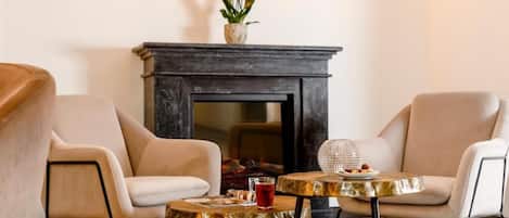 Una habitación con dos sillones, una mesita redonda con una bebida y una chimenea decorada con un florero.