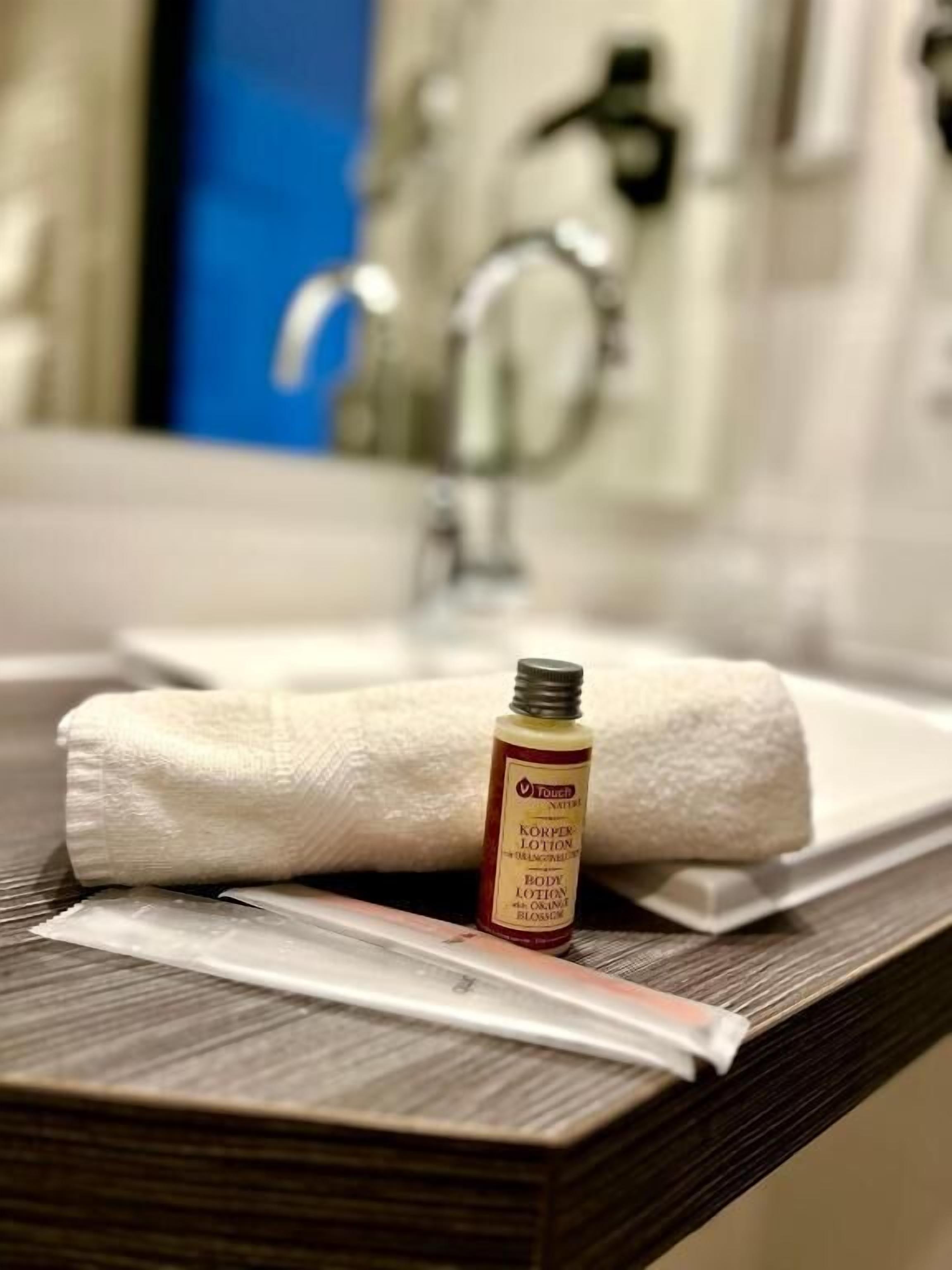 A bathroom with a towel, a bottle of lotion, and a razor on a counter.