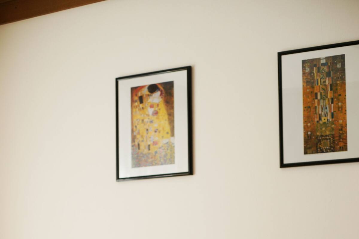 Un lit bien fait, agrémenté d’oreillers à motifs floraux et d’une tête de lit en bois. Deux œuvres d’art encadrées sont accrochées au mur au-dessus du lit.