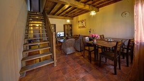 Eine Holztreppe führt zu einem Wohnbereich mit Esstisch und Stühlen, einem Fernseher und einer Uhr an der Wand.