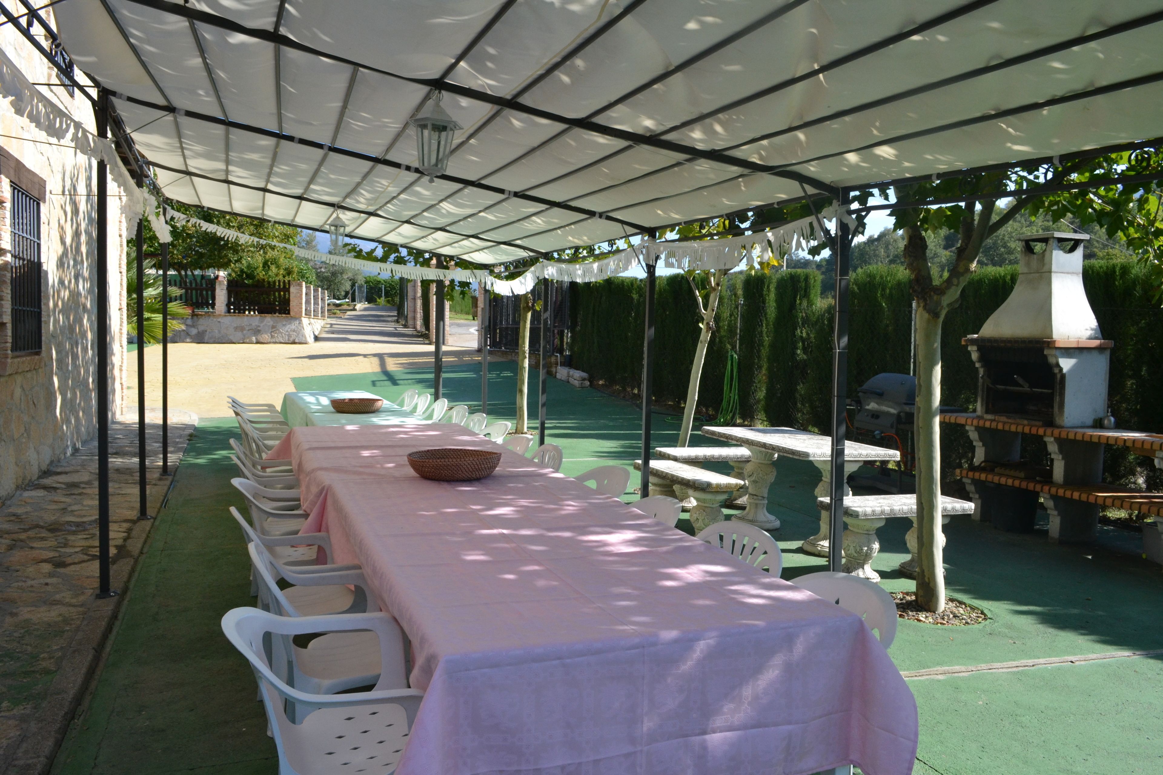 Une terrasse extérieure avec une table et des chaises couvertes, un mur en pierre et un barbecue.