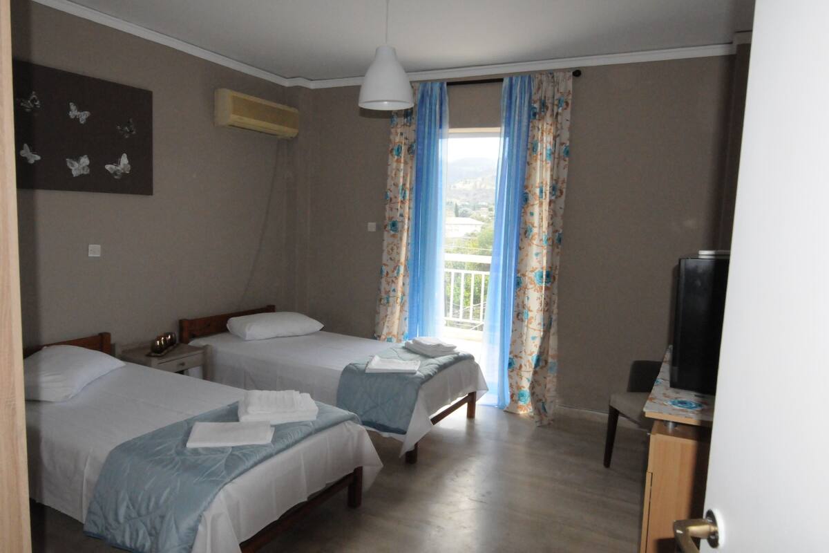Habitación de hotel con dos camas, televisión y balcón con cortinas.