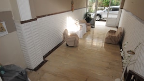 A hallway with a white brick wall, a wooden floor, and a table with chairs. There is a car parked outside. - Kinetta Apartments (Oropos)