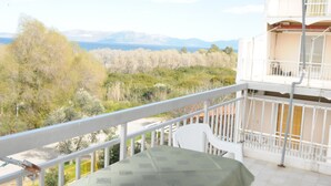 A balcony with a table and chairs, overlooking a landscape with trees and mountains. - Kinetta Apartments (Oropos)