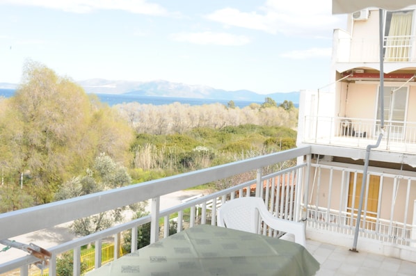 A balcony with a table and chairs, overlooking a landscape with trees and mountains.