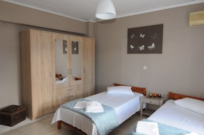 A hotel room with two beds, a wardrobe, a bedside table with a lamp, and a wall-mounted artwork.