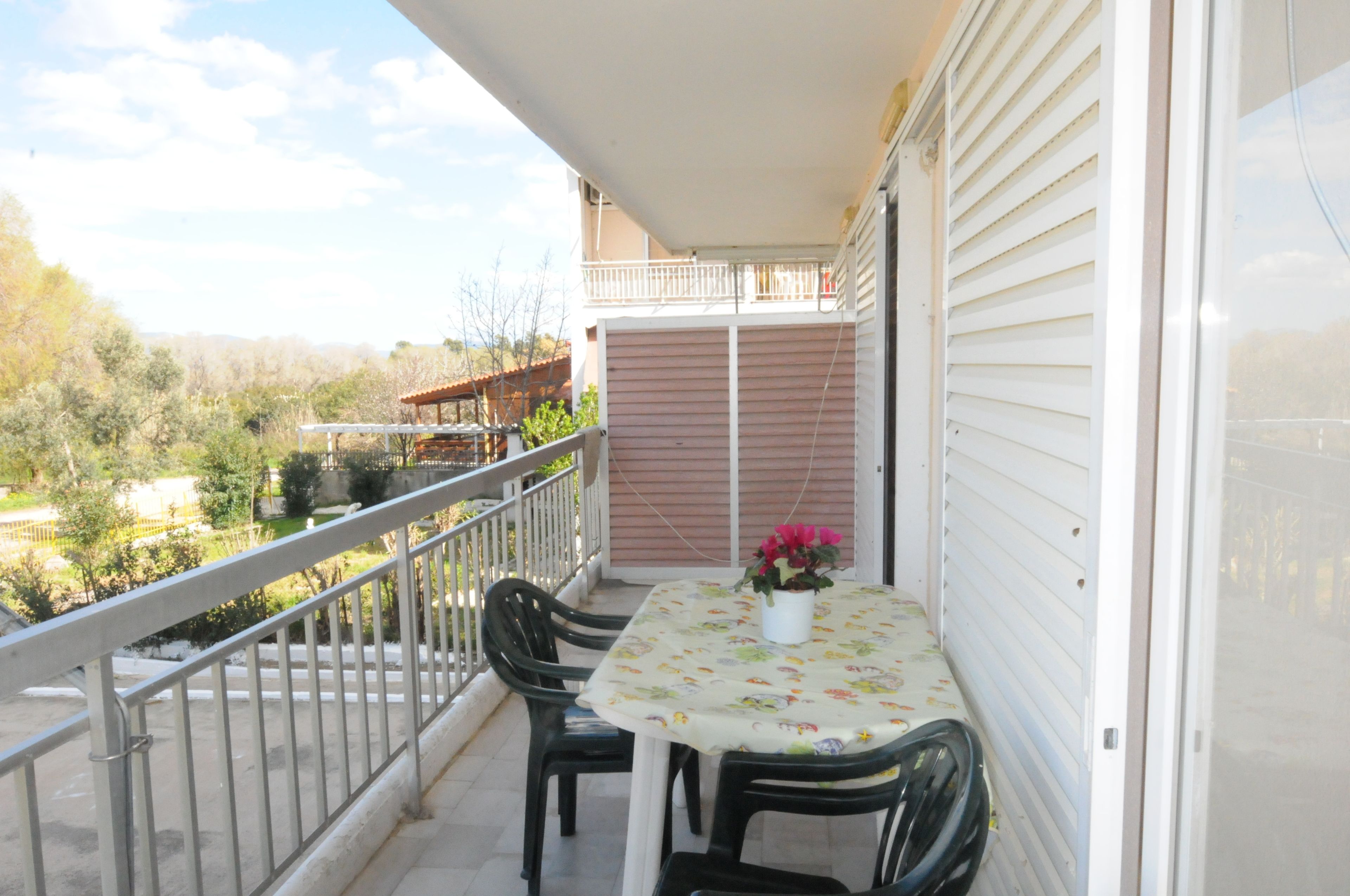 A balcony with a table and chairs, a railing, and a view of the surrounding area.