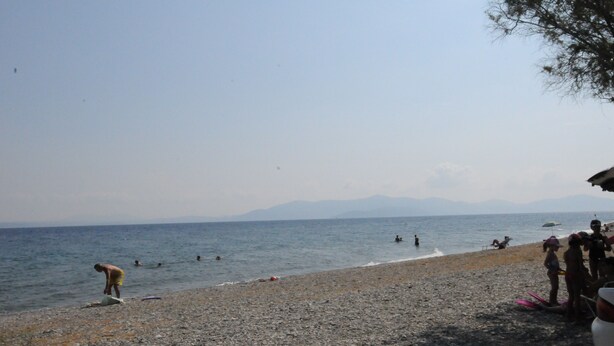 A pebbled beach with people swimming and sunbathing. - Kinetta Apartments (Oropos)