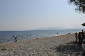 A pebbled beach with people swimming and sunbathing. - Kinetta Apartments (Oropos)