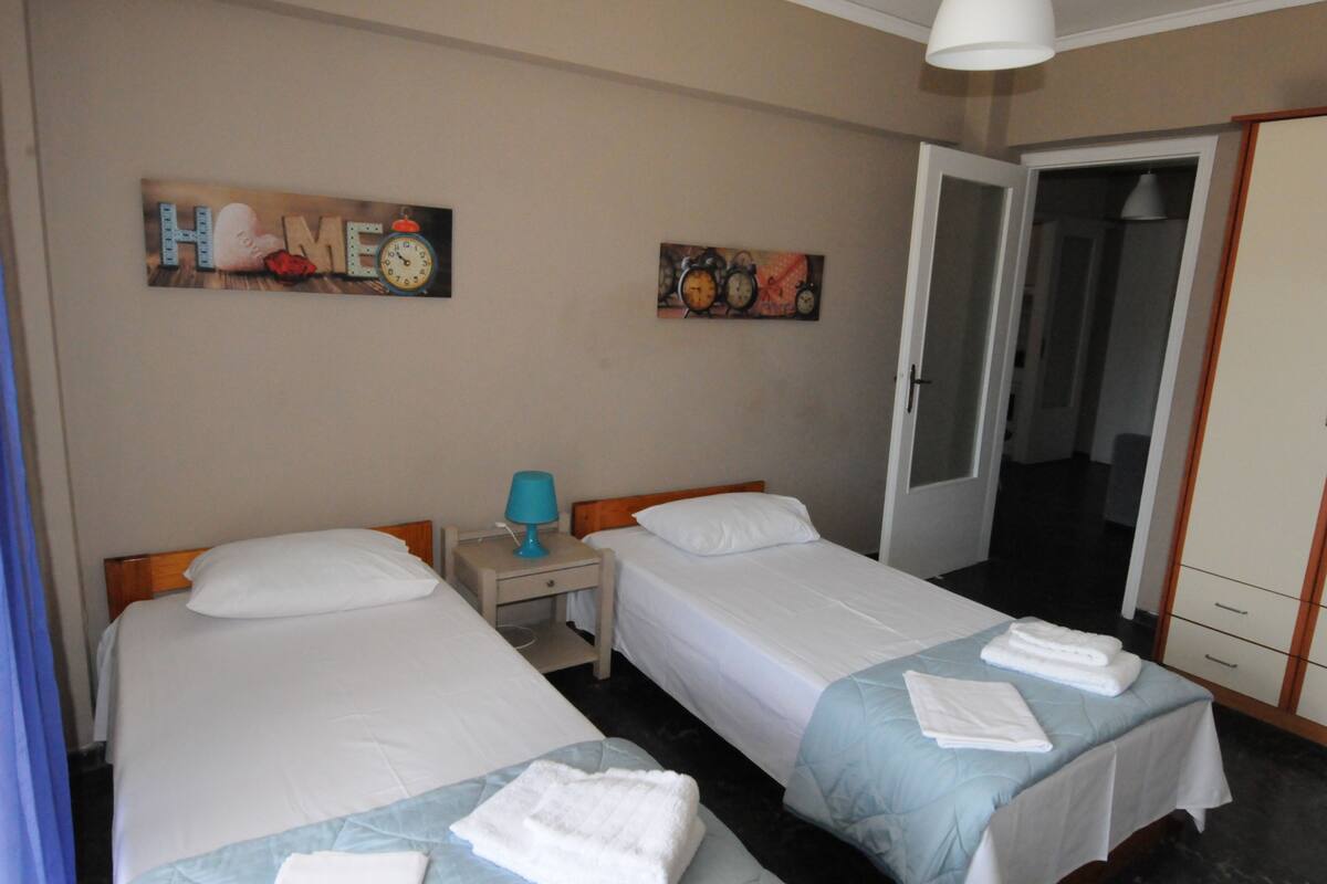 Una habitación de hotel con dos camas, una mesita de noche con una lámpara y una puerta que da a un armario.