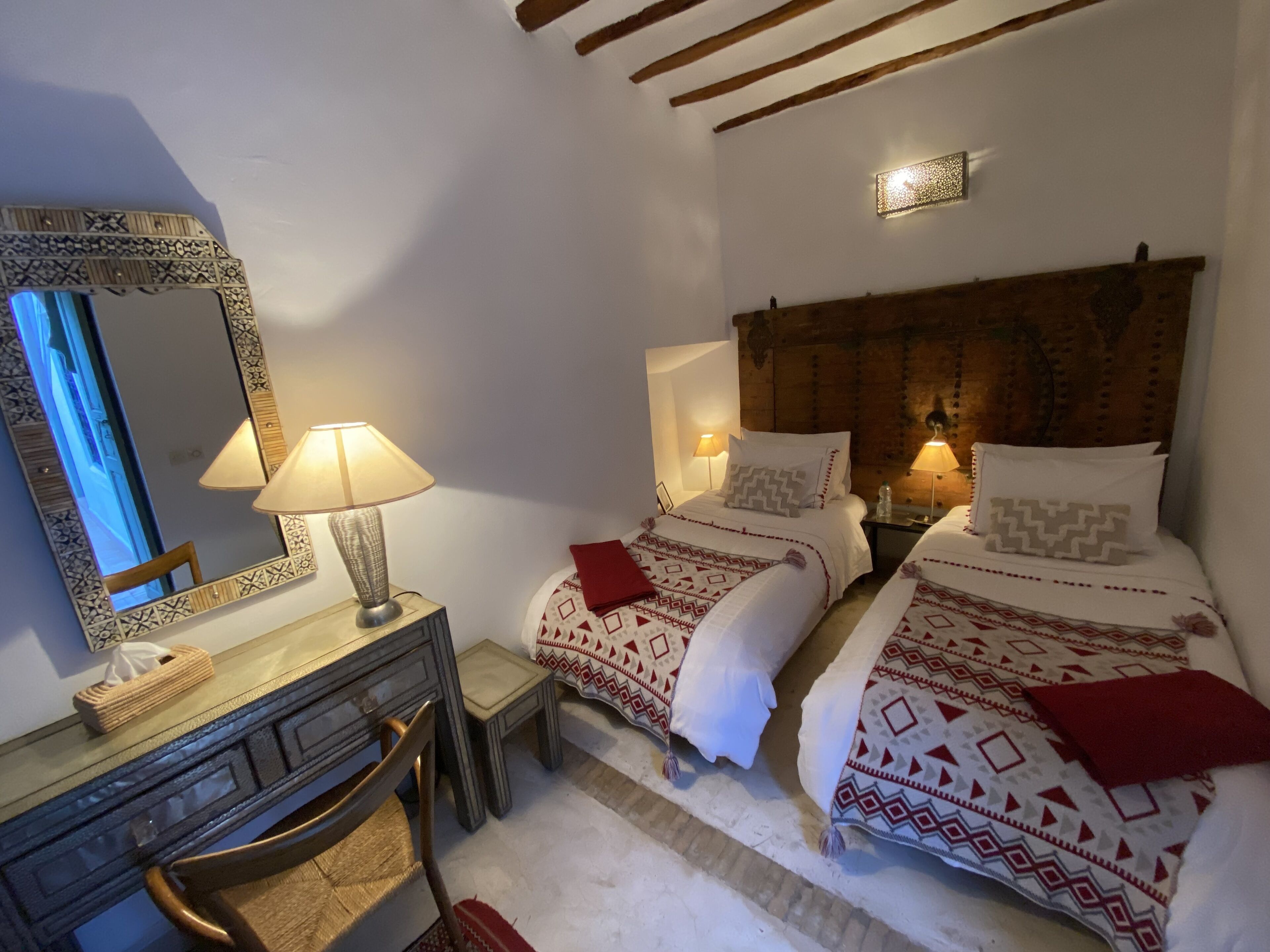 A bedroom with two beds, a dresser, a mirror, and a lamp.