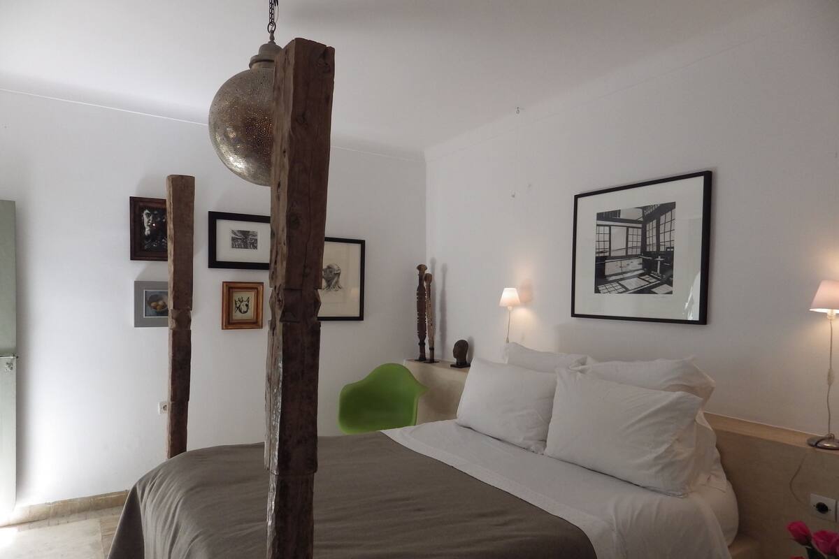 Un dormitorio con una cama, una silla verde y cuadros en la pared.