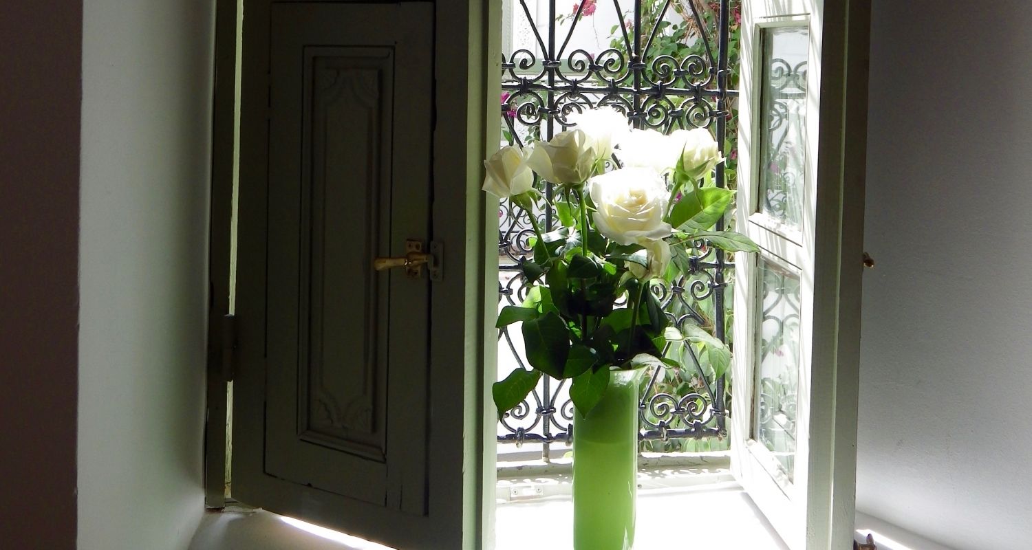 Uma porta com maçaneta de latão, um vaso verde com flores brancas e um portão de ferro forjado ao fundo.