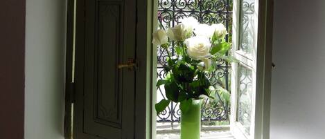 Uma porta com maçaneta de latão, um vaso verde com flores brancas e um portão de ferro forjado ao fundo.