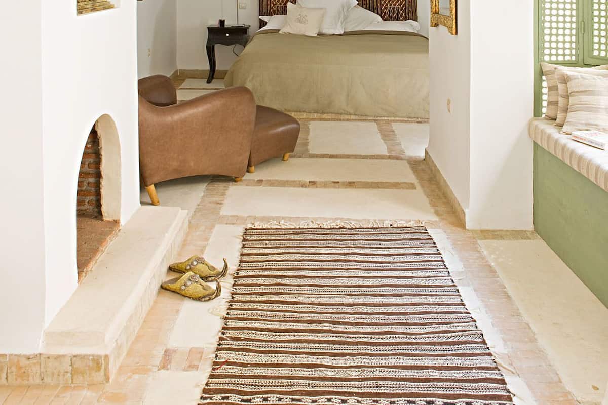 Un dormitorio con cama, lámpara colgante, cabecera estampada y una puerta verde.