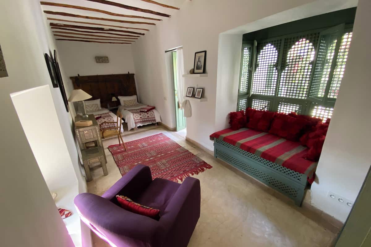 Una habitación con cama, sofá, silla y ventana con diseño de celosía.