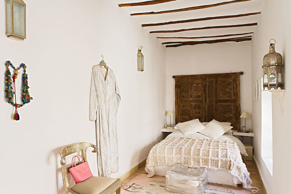 Un dormitorio con cama, una silla, una prenda colgando y un adorno en la pared.
