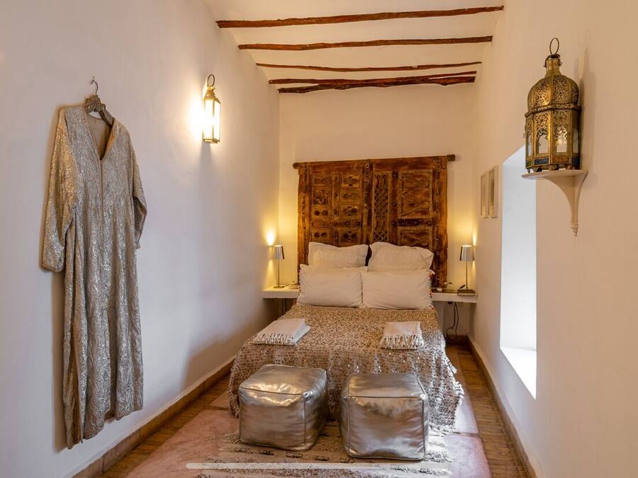 Un dormitorio con cama, dos mesitas de noche, un perchero y un farol decorativo.