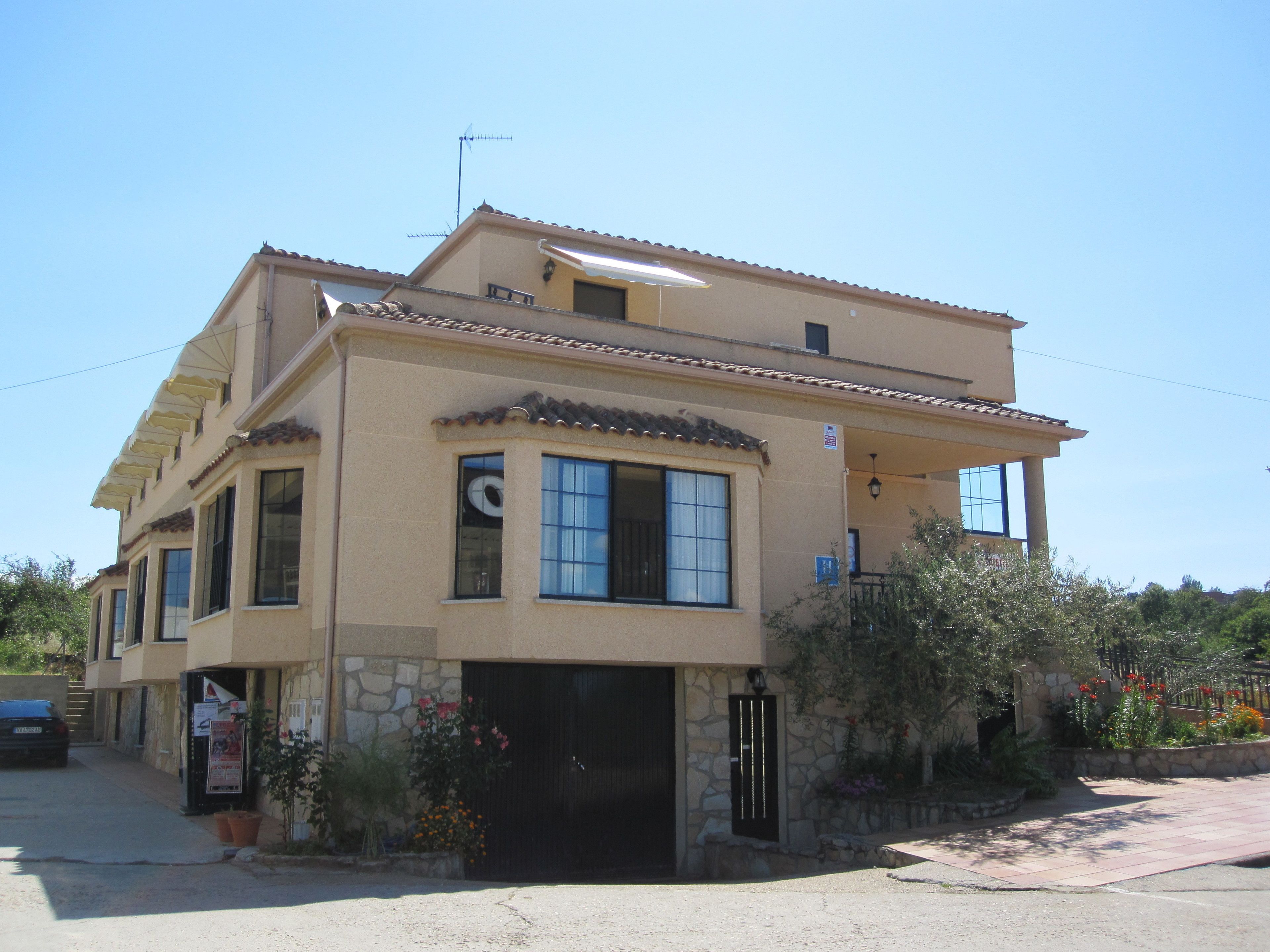 A two-story building with a stone facade, a black garage door, and a small balcony.