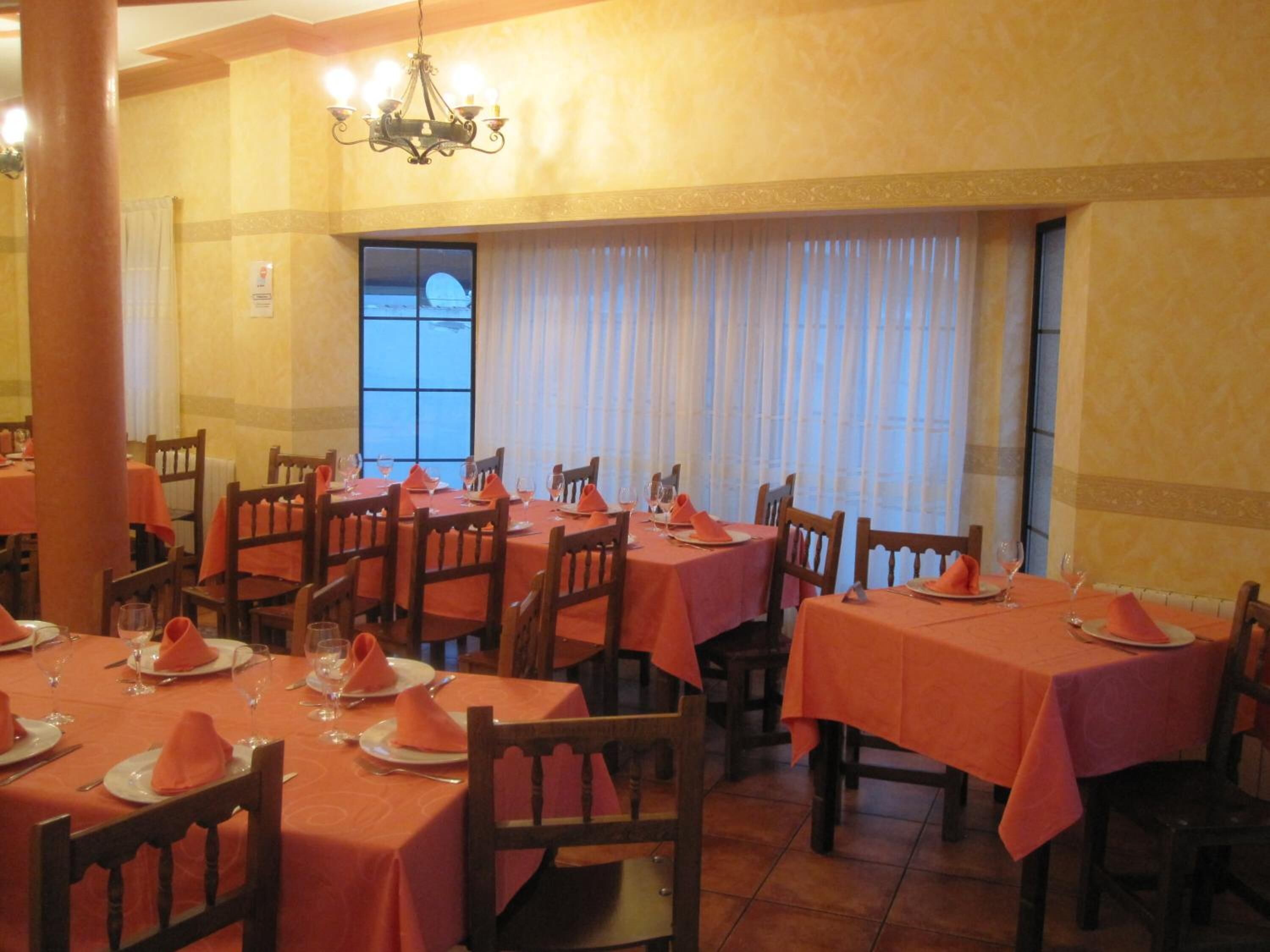 A dining area with tables set for four, each with orange tablecloths and napkins.