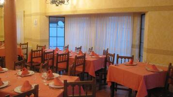 A dining area with tables set for four, each with orange tablecloths and napkins.