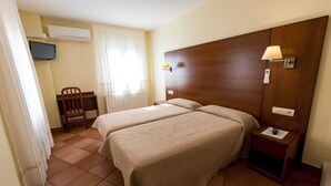 Habitación de hotel con dos camas, cabecera de madera, mesita de noche con lámpara, televisor montado en la pared y ventana con cortinas.