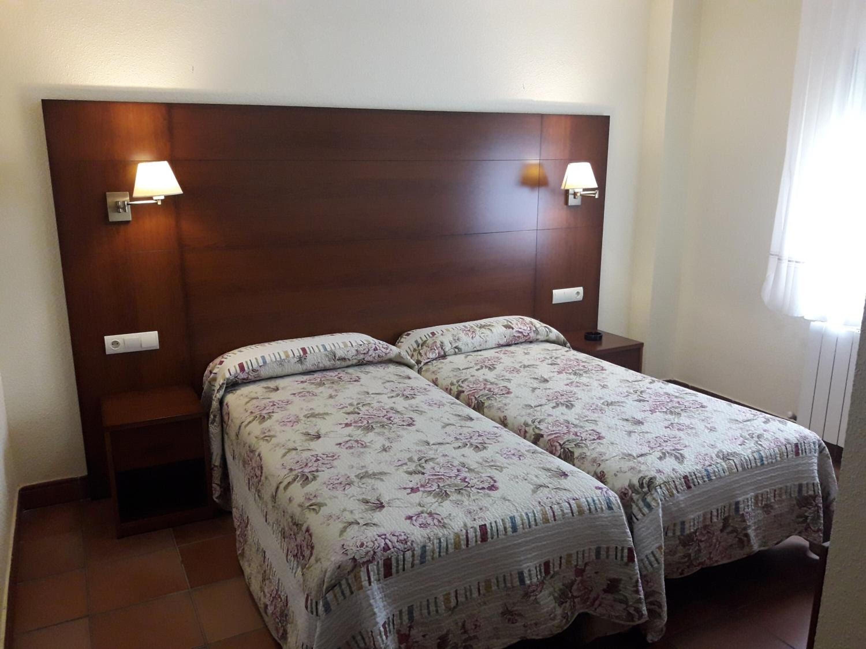 Cama doble con ropa de cama floral, dos lámparas de noche y cabecera de madera en una habitación de hotel.