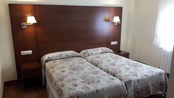 Cama doble con ropa de cama floral, dos lámparas de noche y cabecera de madera en una habitación de hotel.