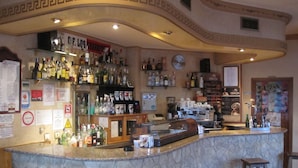 Zona de bar con mostrador de piedra, taburetes y diferentes botellas y vasos.